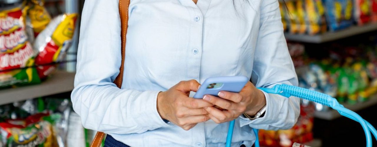 Latin American woman shopping at a convenience store following a shopping list on her cell phone